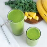 completed Kale Pineapple Smoothie in two glass cups with ingredients in the background