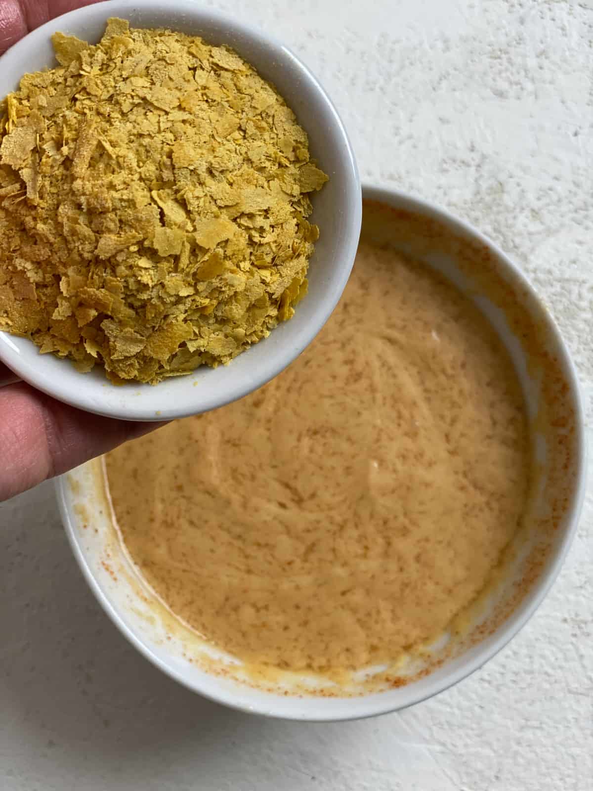 process shot of adding nutritional yeast to sauce mixture in bowl