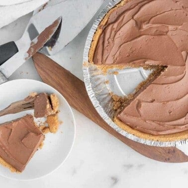 completed chocolate pie with a slice missing and plated on white surface