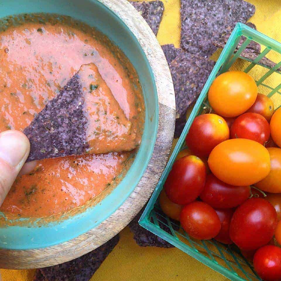 A hand dipping a blue corn chip into a bowl of summer salsa.