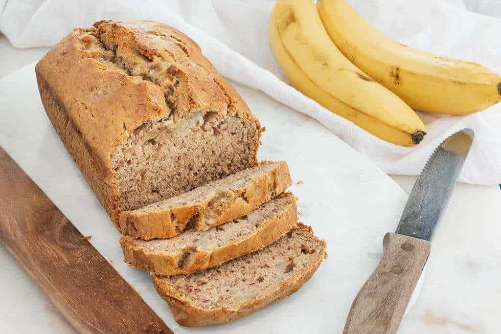 Loaf of vegan banana bread being sliced on a marble board.