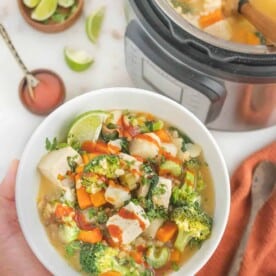 Barley vegetable soup in a white bowl next to a full Instant Pot.