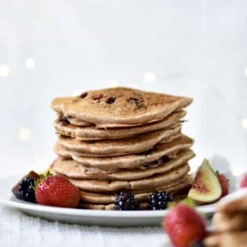 A stack of berry pancakes with fresh fruit on a white plate.