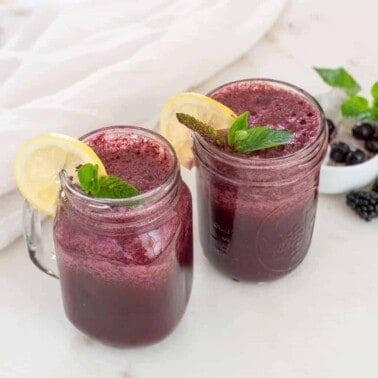 completed Mixed Berry Smoothie Recipe with Mint in two glass jars against a light surface