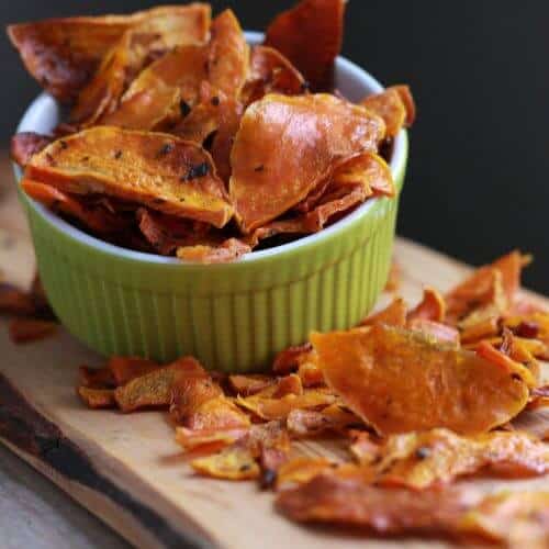 Butternut squash chips in a green bowl on a wood board.