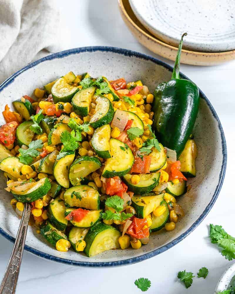 calabasitas recipe with a mixture of veggies in a white bowl with blue rim in a white background