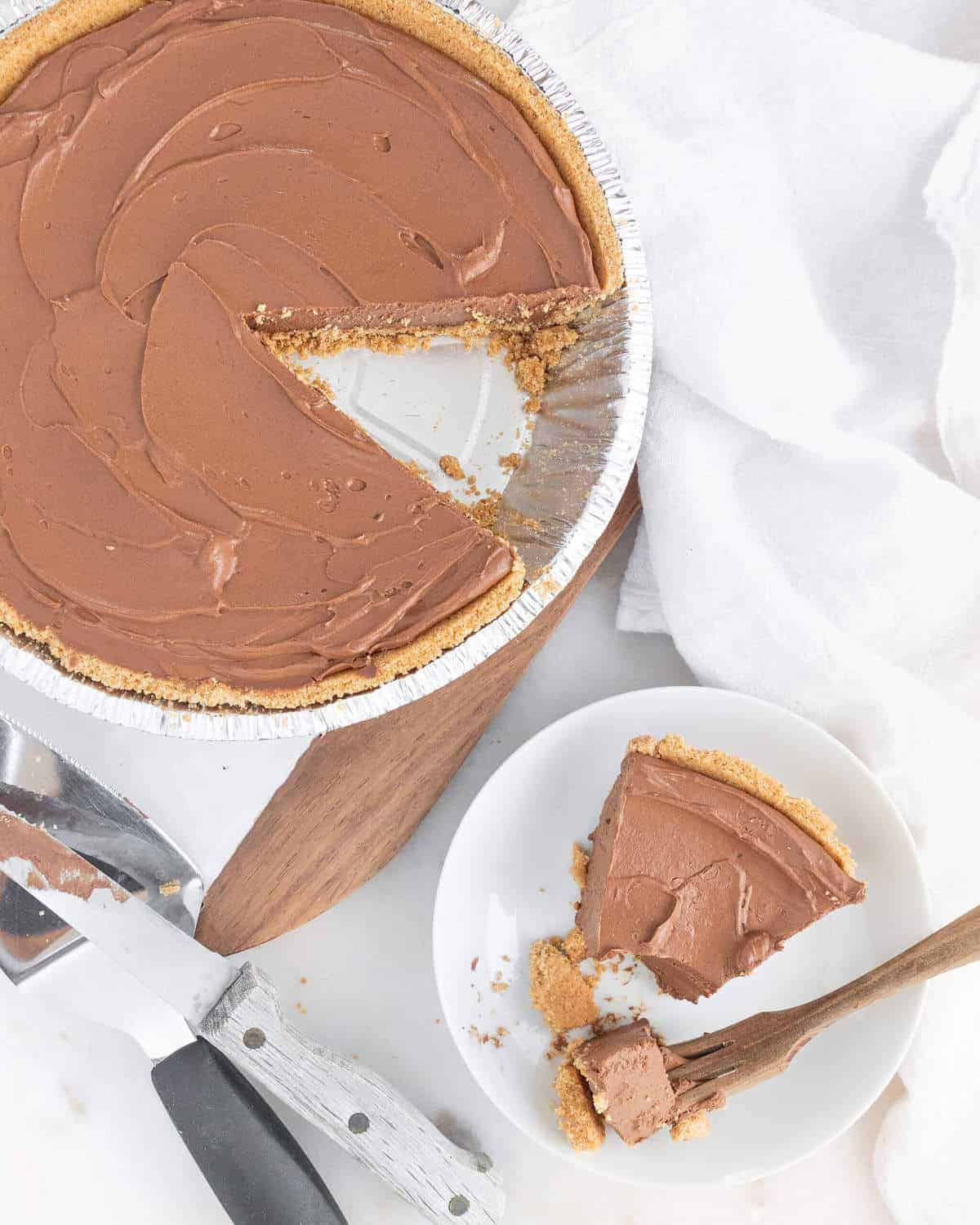 completed chocolate pie with a slice missing and plated on white surface