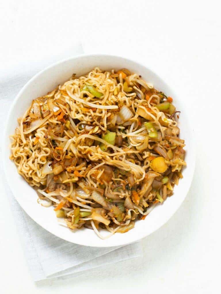 A large white serving bowl filled with fresh made veggie chow mein.