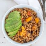 Quinoa and sweet potato chili topped with avocado in a white bowl.
