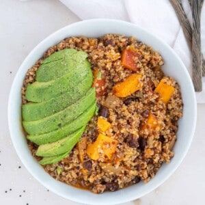 Quinoa and sweet potato chili topped with avocado in a white bowl.
