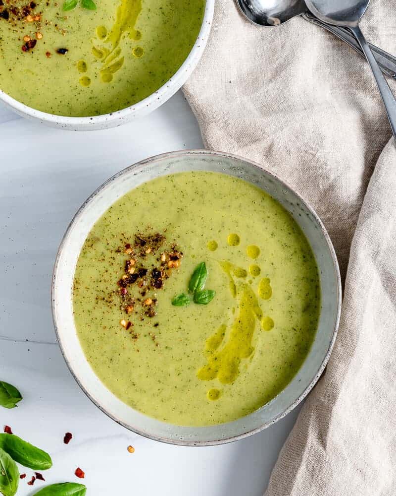 Creamy vegan zucchini basil soup in two small bowls.