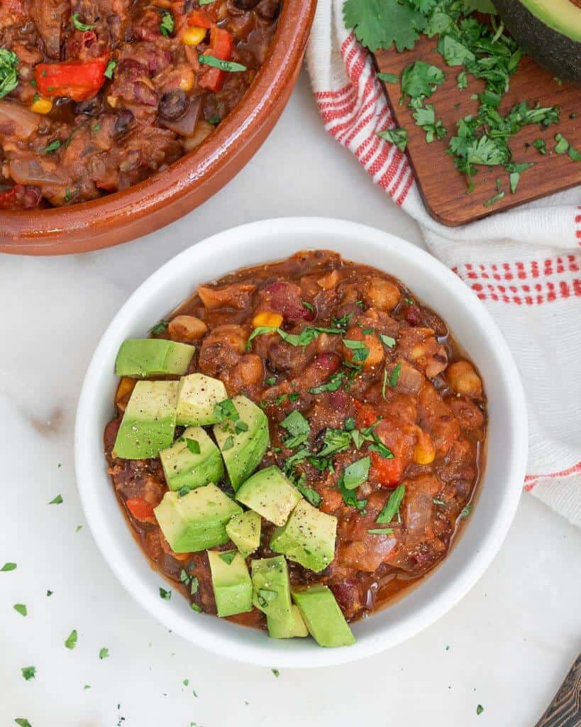 a finished bowl of four bean chili topped with avocado against a white background