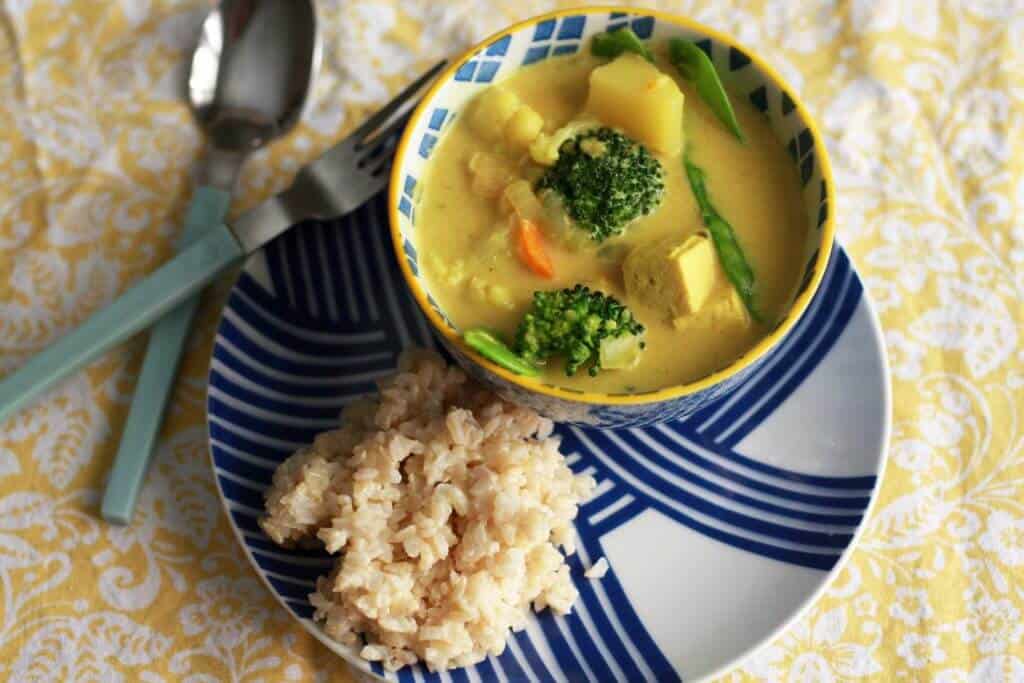 Coconut curry in a small bowl next to rice on a plate.