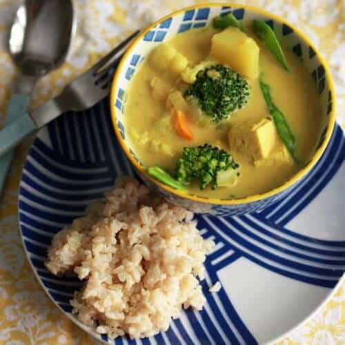 Coconut curry in a small bowl next to rice on a plate.