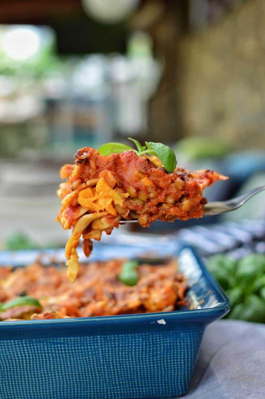 A fork holding up a bite of sweet potato lasagna over a full blue baking dish.