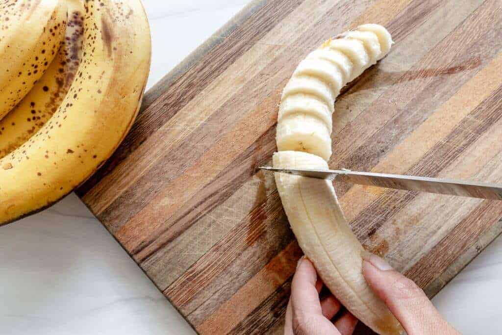 A banana being sliced on a wood board.