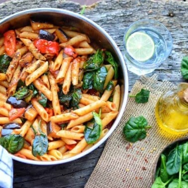 finished Eggplant Penne in a dish with ingredients spread out against a dark background