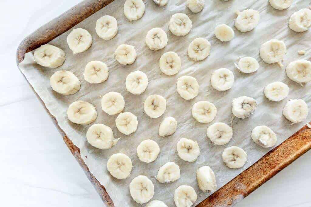 Frozen banana slices on a parchment-lined baking sheet.