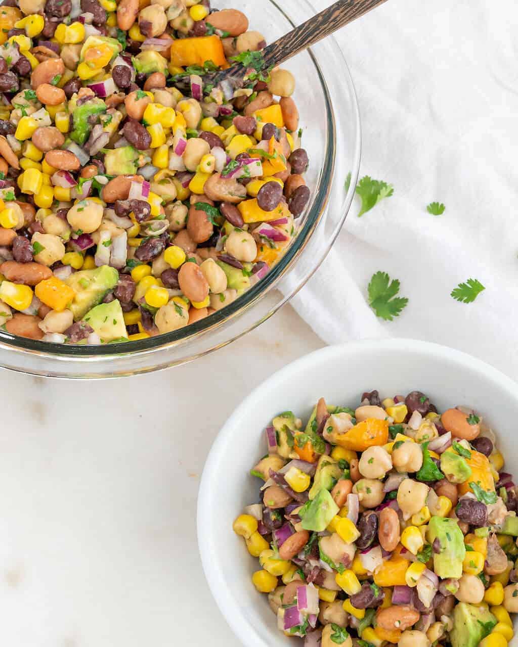 Clear mixing bowl filled with bean salad and a serving in a small white bowl.
