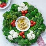 Fresh green vegetables arranged like a wreath around a bowl of dip.