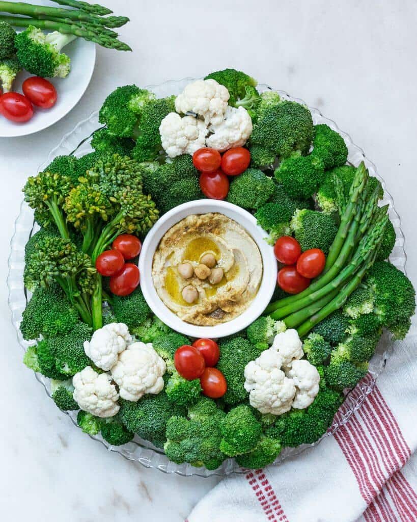 Fresh green vegetables arranged like a wreath around a bowl of dip.