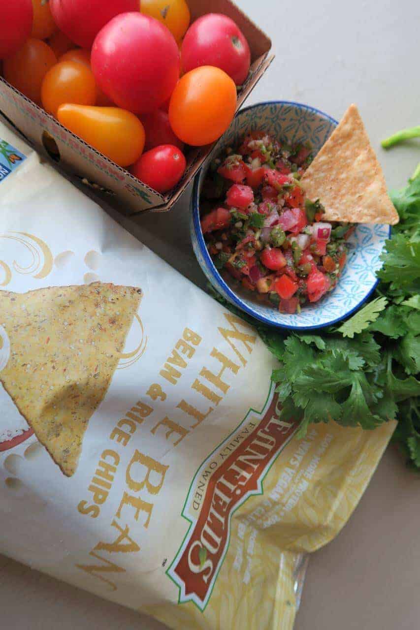A box of tomatoes, a bowl of pico de gallo and a bag of tortilla chips.