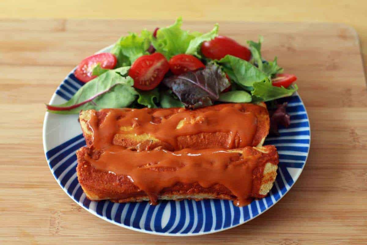 Two sweet potato enchiladas and a green salad on a dinner plate.