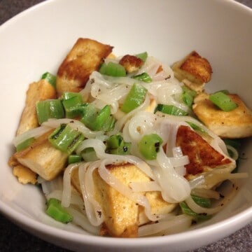 Mustard greens, tofu, and rice noodles in a bowl.