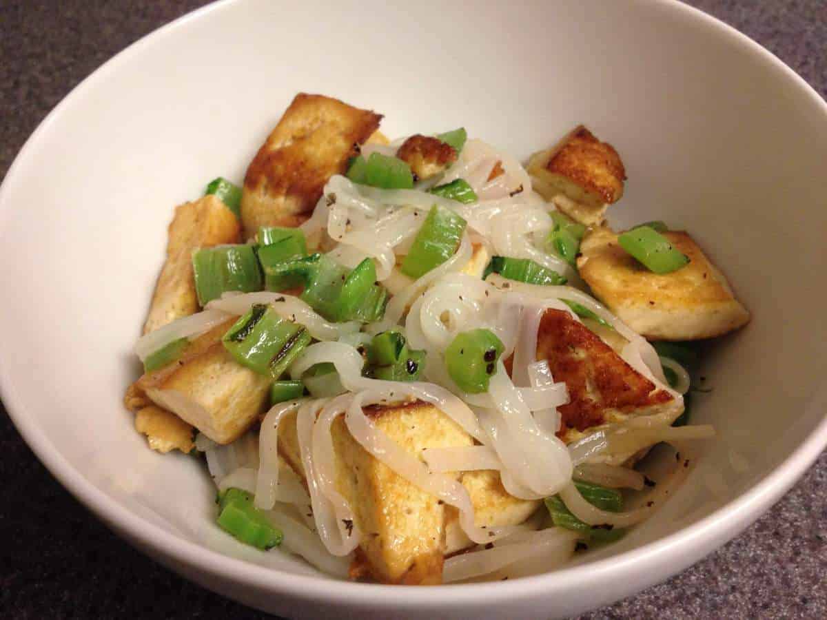 Mustard greens, tofu, and rice noodles in a bowl.