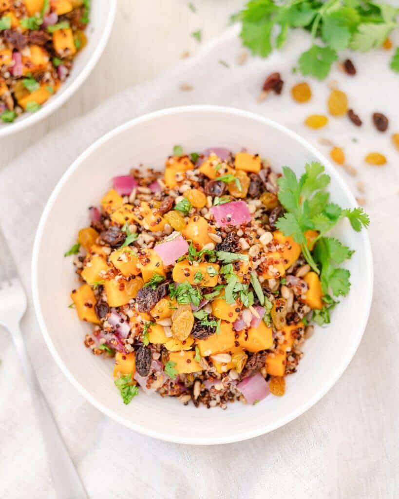 finished sweet potato quinoa salad in a white bowl with incredients spread out against a white background