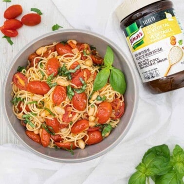 finished Tomato Basil Pasta in a gray bowl with product and ingredients against a white background