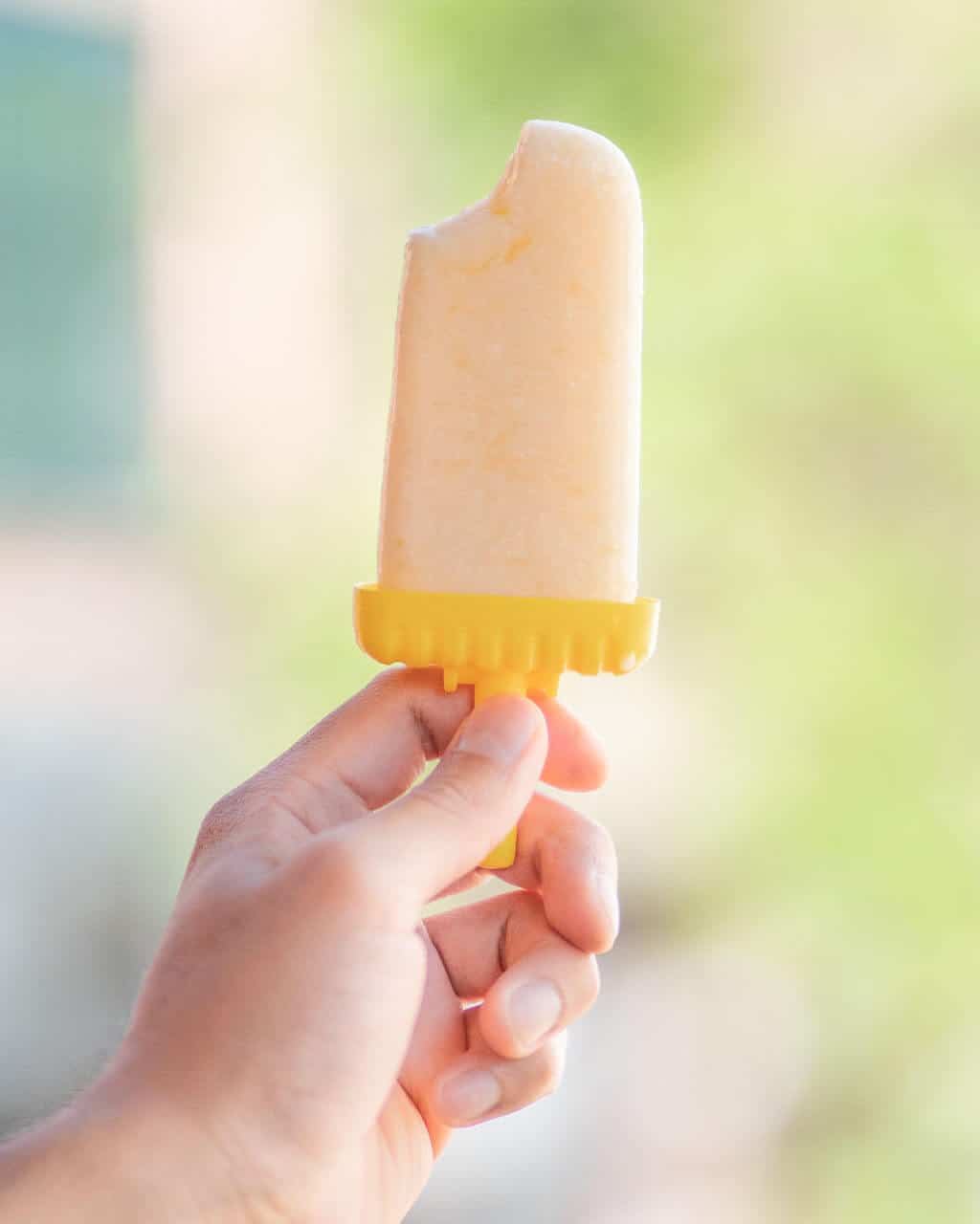 one completed lemon ice pop held in a hand with a bite missing from it