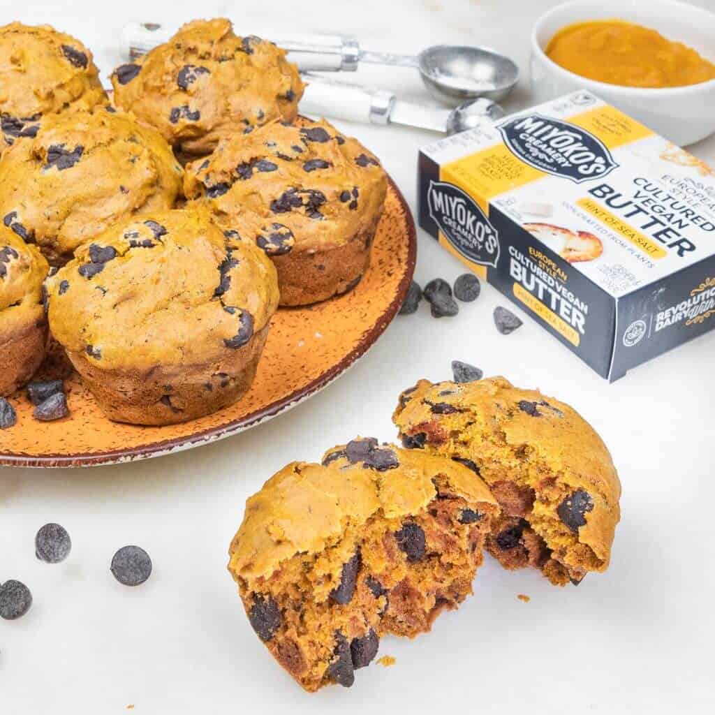 several pumpkin muffins on an orange plate with a split muffin the the forefront against a white background