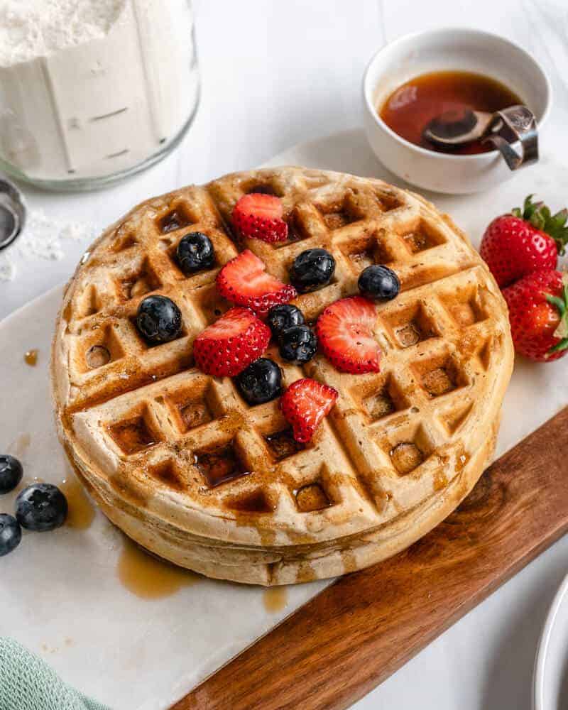 stack of waffles on a white and brown surface with berries and syrup on the side