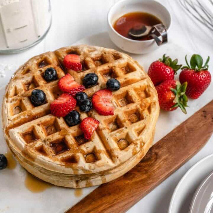 stack of waffles on a white and brown surface with strawberries and blueberries on the side