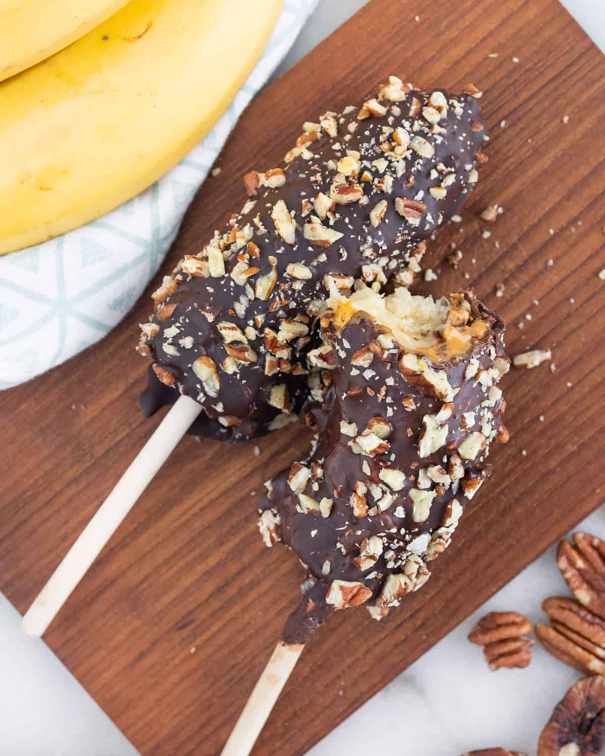 Chocolate covered peanut butter bananas on a wood board.