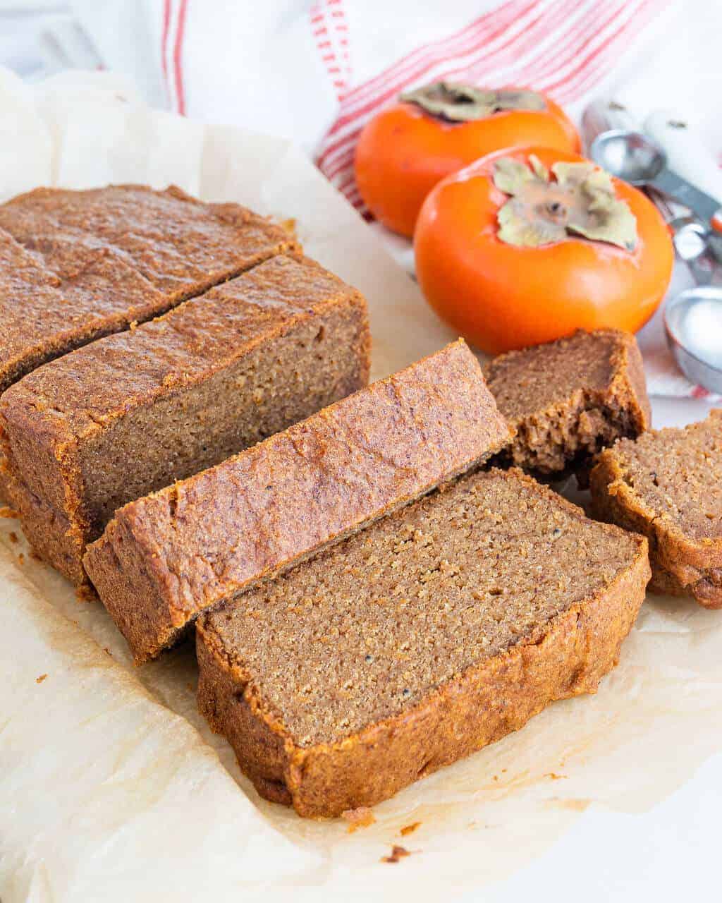 persimmon bread slices on a white surface with persimmons in the background