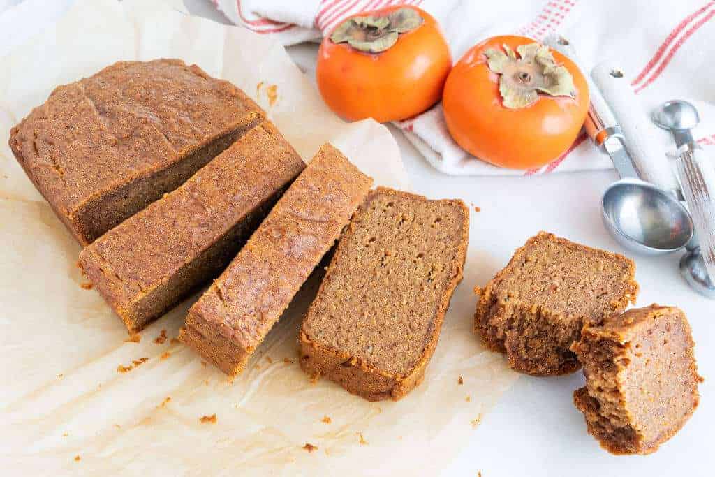 persimmon bread slices on a white surface with persimmons in the background