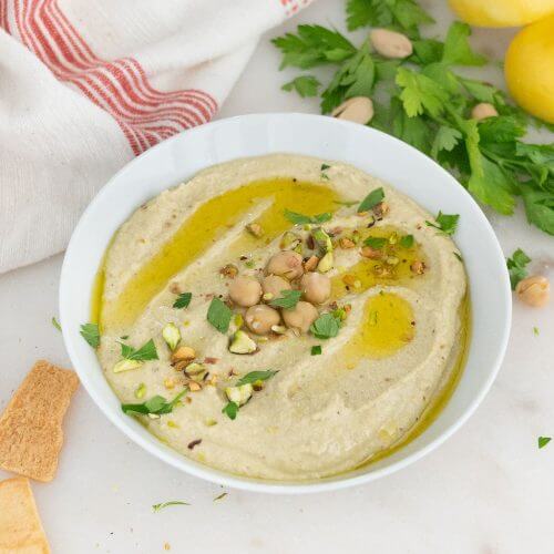 A bowl of pistachio hummus topped with cilantro and olive oil.