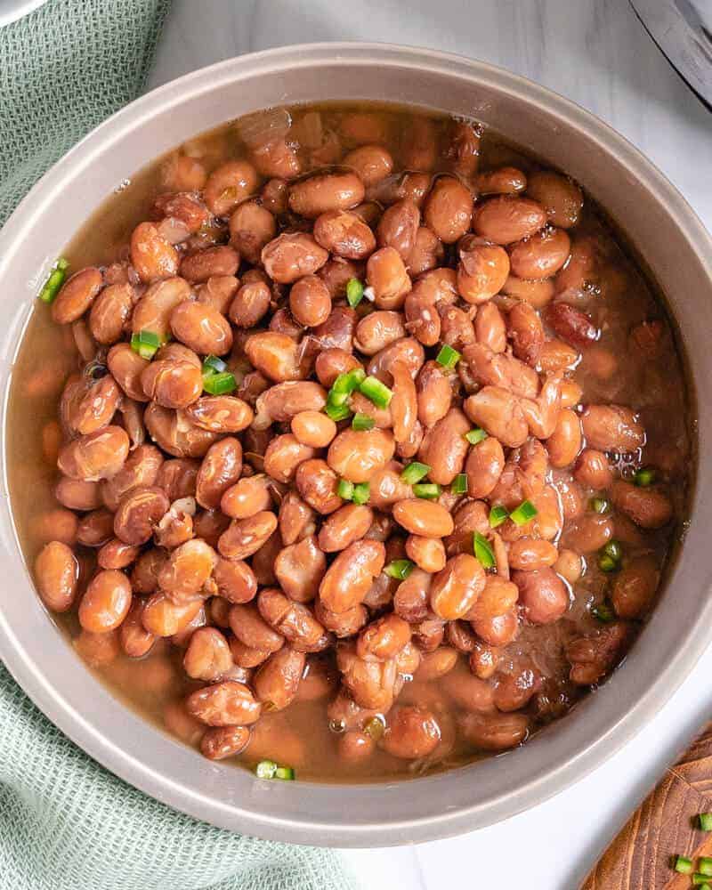 completed pinto beans in a bowl against a white counter with a light green cloth and brown cutting board in the background
