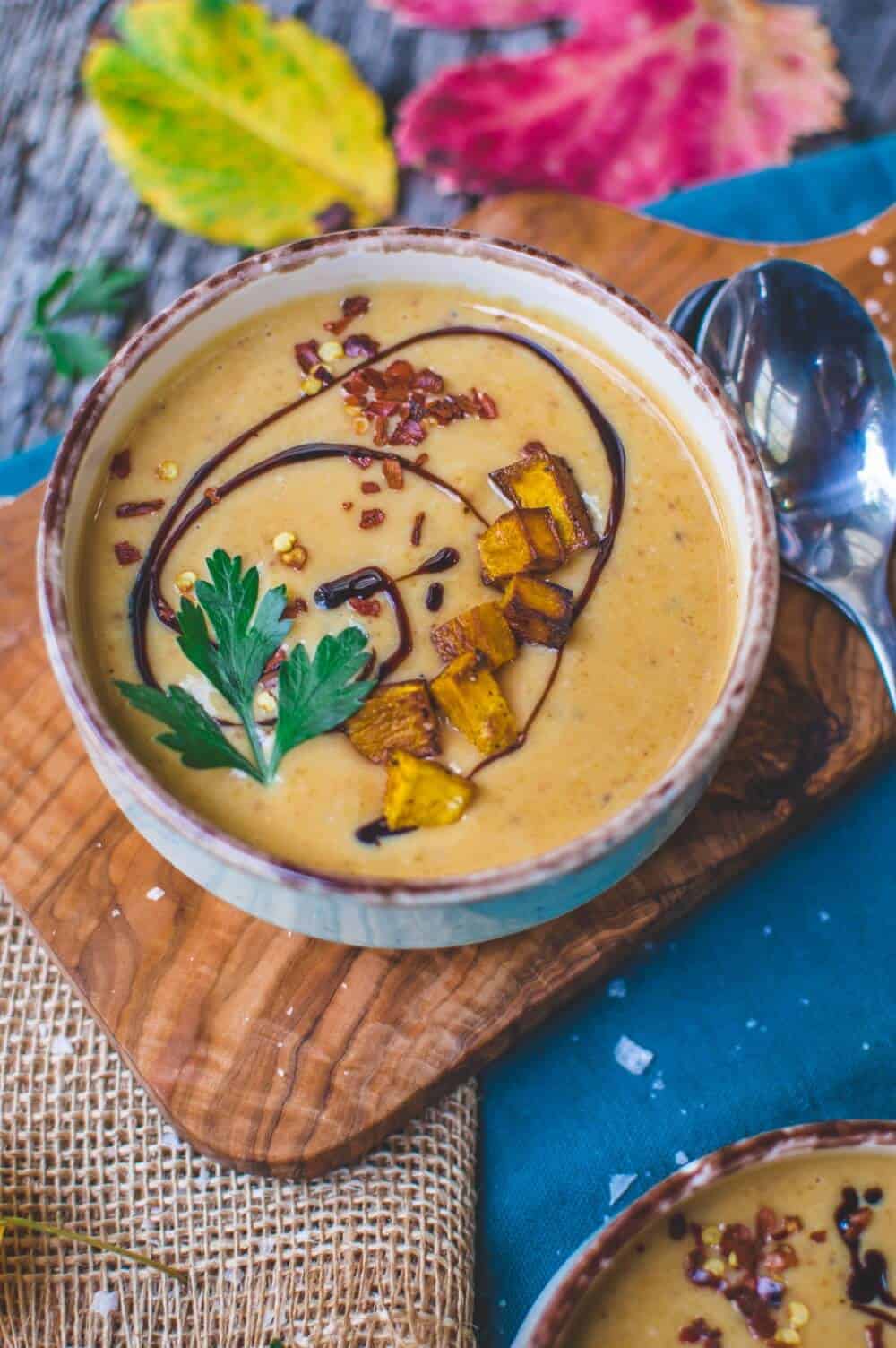 Top view of a bowl of vegan pumpkin soup on a wood board.