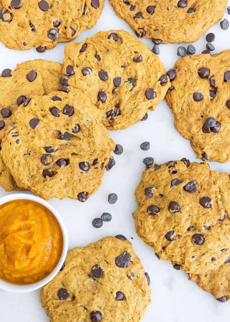 several finished pumpkin chocolate chip cookies scattered on a white surface