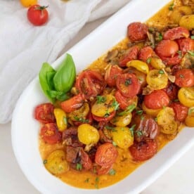 A white oblong platter filled with roasted cherry tomatoes.