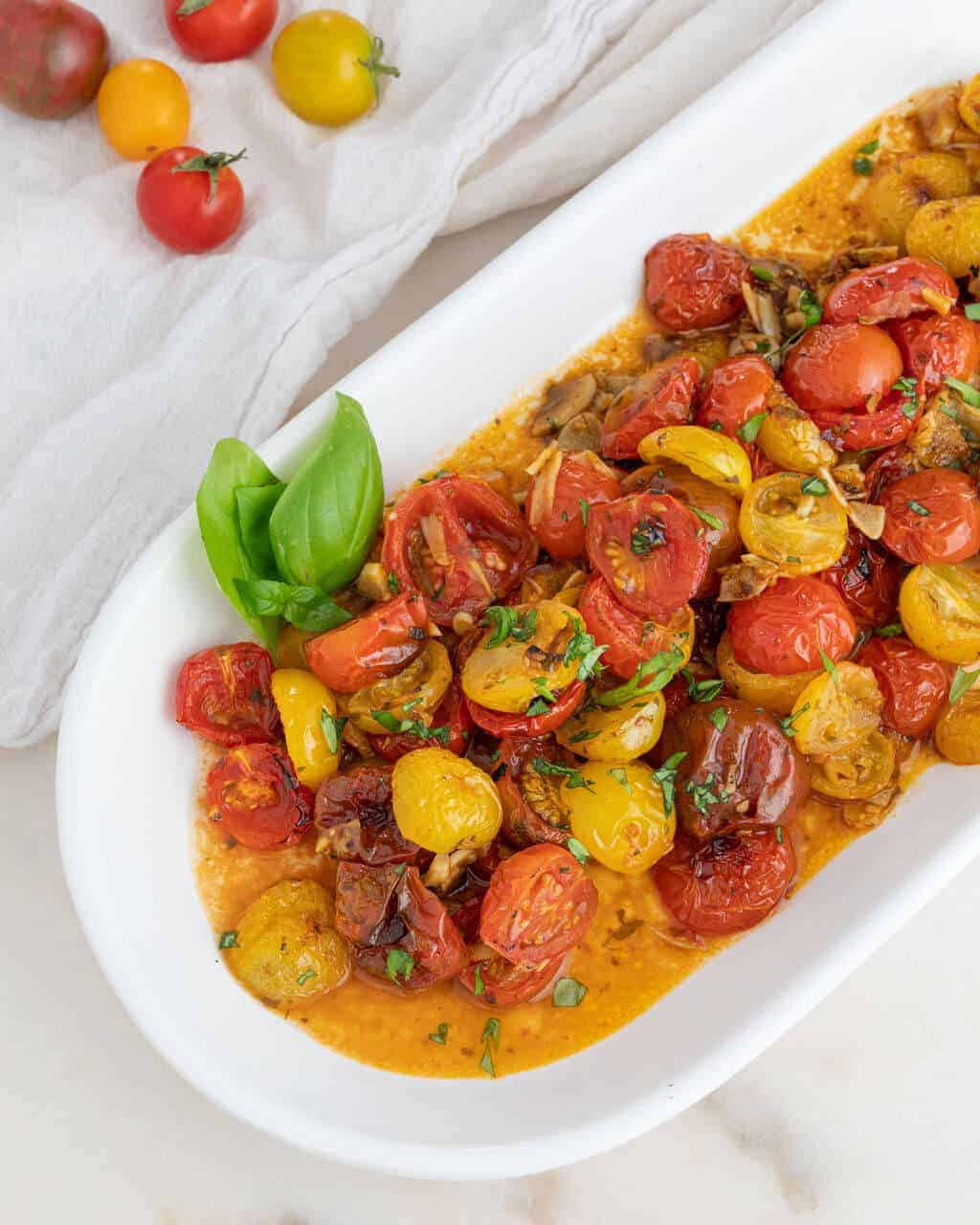A white oblong platter filled with roasted cherry tomatoes.