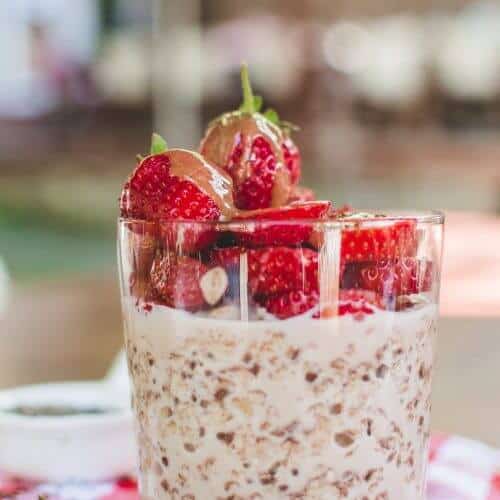 Side view of a glass of overnight oats topped with fresh strawberries.