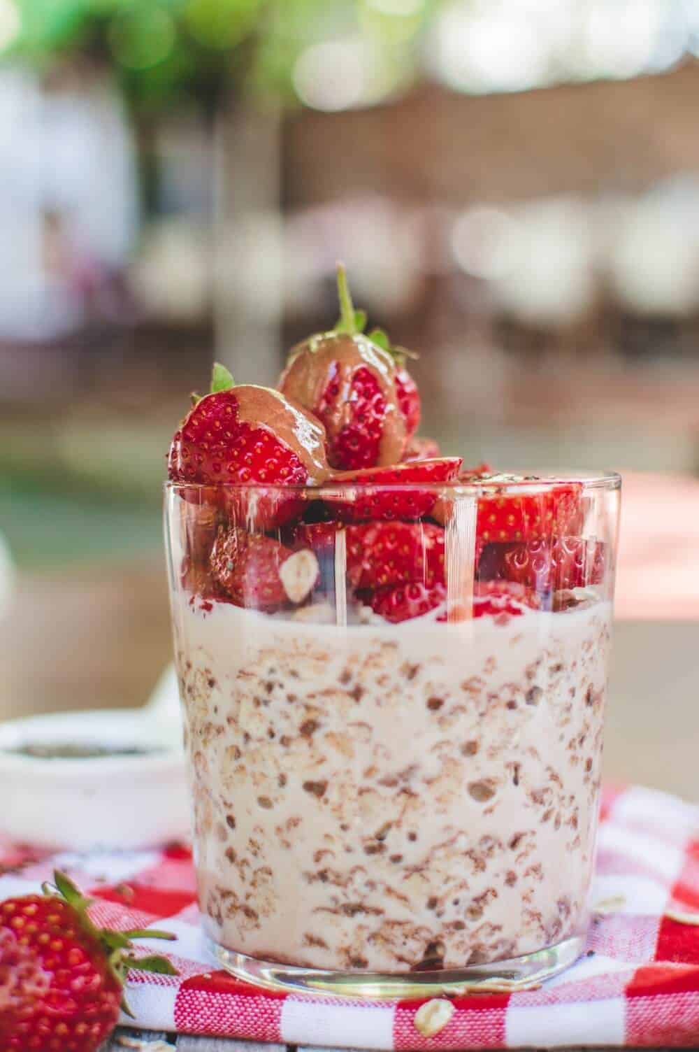 Side view of a glass of overnight oats topped with fresh strawberries.
