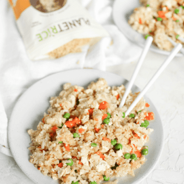 A large bowl of brown rice fried rice with a pair of chopsticks in it.