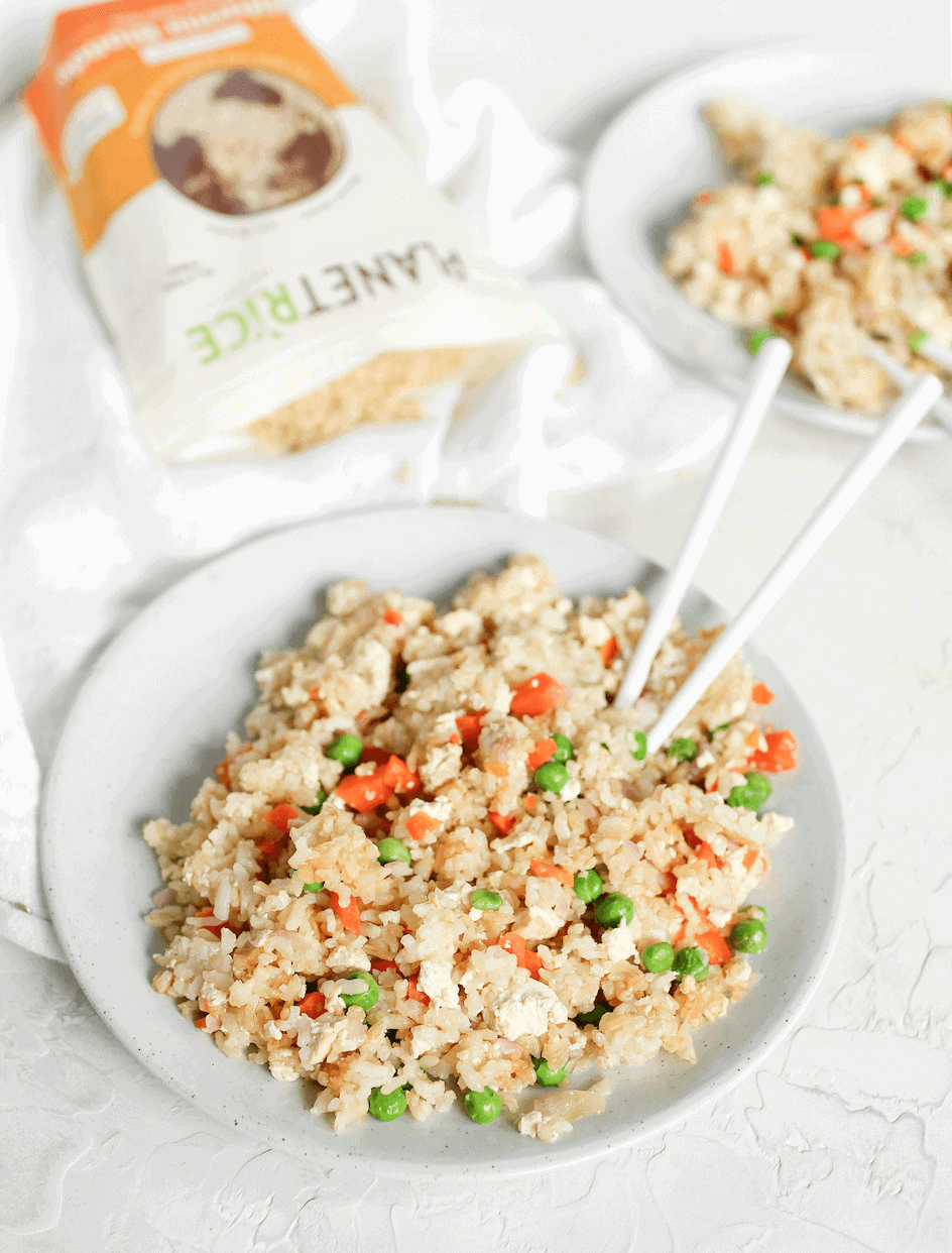 A large bowl of brown rice fried rice with a pair of chopsticks in it.