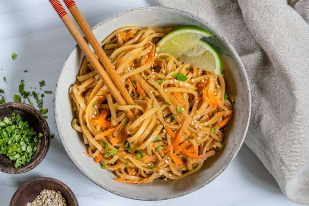 finished Sesame Noodle Salad plated in a white dish with chopsticks against a white background 