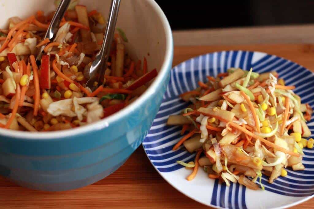 Serving bowl of vegan slaw next to a serving on a plate.